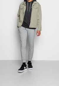 Grön denimjacka över en mörk huvtröja, grå sweatpants och svarta sneakers med vita detaljer. Avslappnad outfit lämplig för lager-på-lager.