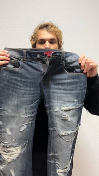 Slitna blå jeans i denim med flera revor och blekta partier, utrustade med knappgylf, design med fem fickor och en röd etikett i midjebandet.
