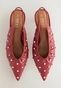 Punaiset nahkaiset slingback-kengät, joissa on terävä kärki, ryppyinen muotoilu ja hopeakoristeet. Sisällä näkyy logotunnistus.
