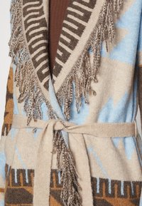 Lång cardigan i mjukt, texturerat tyg med geometriska mönster i blått, brunt och beige. Fransade kanter och midjebälte.