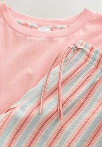 Haut rose pâle à col rond associé à un pantalon à cordon pastel rayé dans des tons de rose, bleu et blanc, présenté à plat.