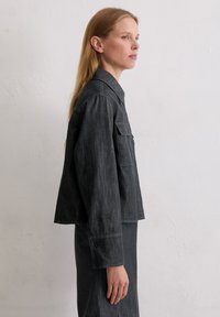 Czarna kurtka dżinsowa o krótkim kroju, z kołnierzem i kieszenią na piersi, teksturowana tkanina oraz zapinane na guziki mankiety. Prosty i nowoczesny design.