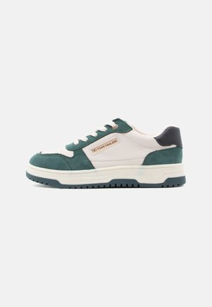 Sneakers featuring a white leather upper with green suede accents and a dark blue heel, contrasted by a ridged white sole.