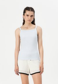 Lyseblå ribbestrikket tank topp med tynne stropper og firkantet utringning, kombinert med hvite teksturerte shorts med svart blonderkant.