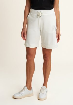 Pantaloni corti bianchi in cotone con vita regolabile, orli arrotolati e un logo decorativo di strass sulla parte anteriore. Abbinati a sneaker bianche.