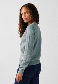 Lichtblauwe sweatshirt met lange mouwen, geribbelde manchetten en een ronde hals. Bevat een klein logo-patch aan de zoom. Gecombineerd met donkere jeans.