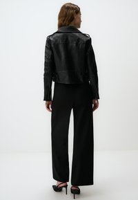 Giacca biker in pelle nera con un design cropped, maniche lunghe e fregi sulle spalle. Abbinata a pantaloni neri a vita alta con gamba ampia e tacchi.