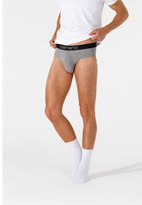 Boxer da uomo grigi con elastico nero con il marchio "camano", indossati sotto una maglietta bianca, su uno sfondo bianco.