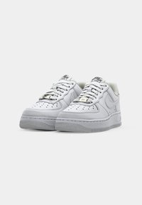 Ett par vita Nike Air Force 1 sneakers med snören, perforeringar på tån och gummisulor på en helt vit bakgrund.