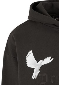 Sweat à capuche noir avec un motif de colombe blanche sur la poitrine et une capuche avec un détail de couture frontale.