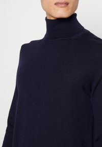 Mörkblå stickad polotröja av fint material, med en tight passform vid halsen och en slät yta. Minimala sömmar synliga.