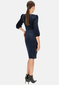 Granatowa koronkowa sukienka z teksturowanym wzorem w panterkę, dopasowana sylwetka, rękawy o długości trzech czwartych oraz długość do kolan, zestawiona z czarnymi botkami za kostkę.
