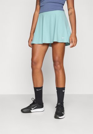Lichtblauwe tennisrok met een uitlopende ontwerp en een elastische tailleband, gecombineerd met een marineblauw top, zwarte Nike sokken en zwarte sportschoenen.