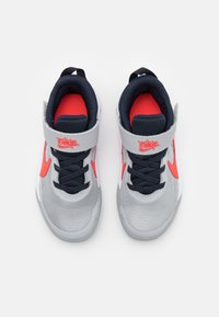 Nike-tennarit, joissa on harmaa verkkomateriaali, tummansiniset yksityiskohdat, kirkas punainen logo ja yksityiskohdat, sekä tarranauhalla ja nauhoilla oleva sulkemismekanismi.