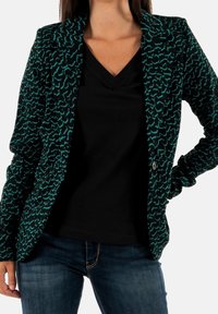 Veste noire texturée avec un motif abstrait bleu sarcelle, dotée d'un col cranté et d'une fermeture à un bouton. Portée sur un haut noir à col en V.