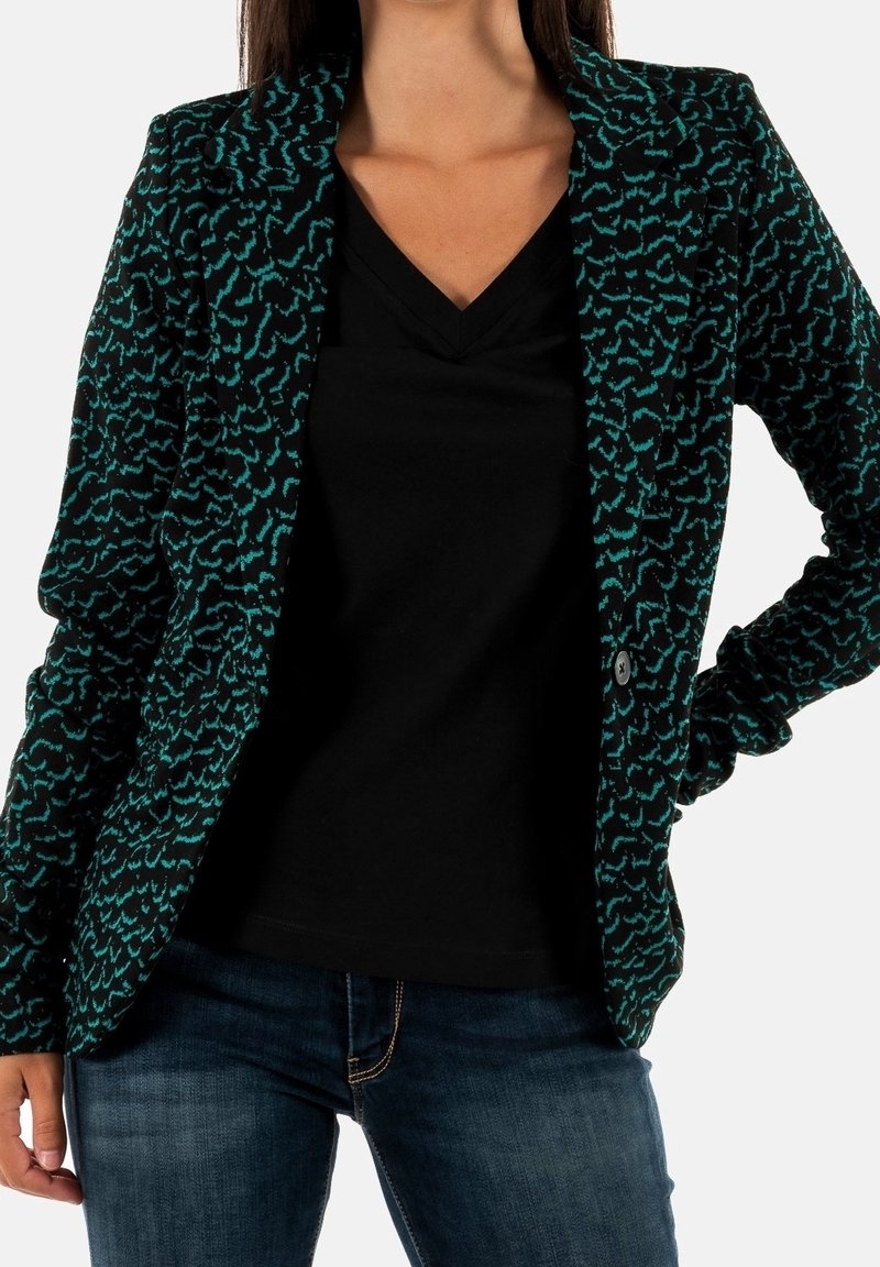 Veste noire texturée avec un motif abstrait bleu sarcelle, dotée d'un col cranté et d'une fermeture à un bouton. Portée sur un haut noir à col en V.