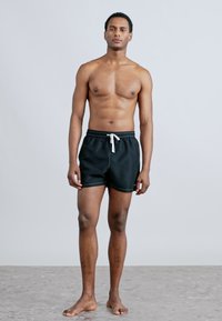 Μαύρα μαγιό βερμούδα με κορδόνι στη μέση, διαθέτοντας λευκή ραφή και πλαϊνές τσέπες. Απλό σχέδιο, ελαφρύ ύφασμα.