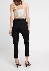 Černé slim-fit kalhoty s hladkou texturou, se středním pasem a nenápadnými zadními kapsami, doplněné lehkým satinovým topem na ramínka.