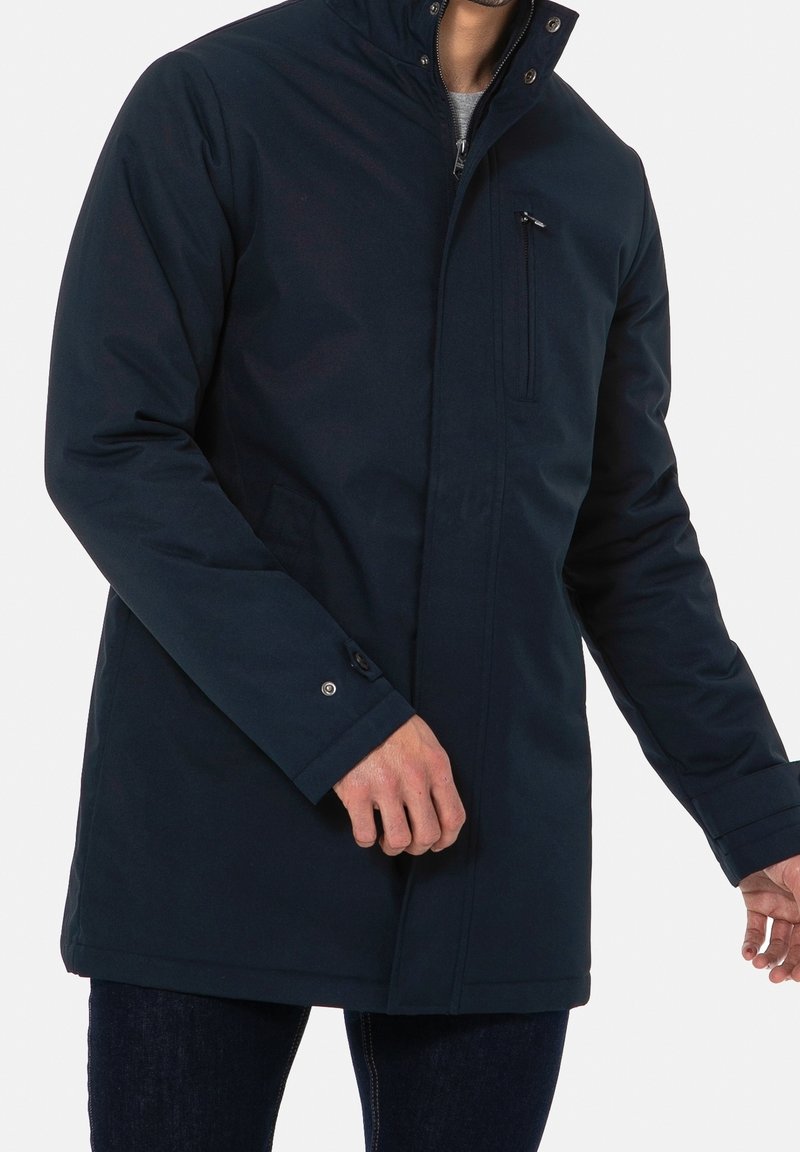 Cappotto impermeabile blu navy con alto colletto, zip frontale e tasca sul petto. Presenta polsini con bottone a scatto e una silhouette snella.
