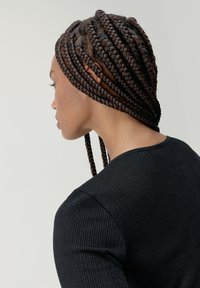 Top negro de canalé con un escote redondeado. Cabello peinado en trenzas largas y ordenadas que caen planas sobre el cuero cabelludo y cuelgan por la espalda.