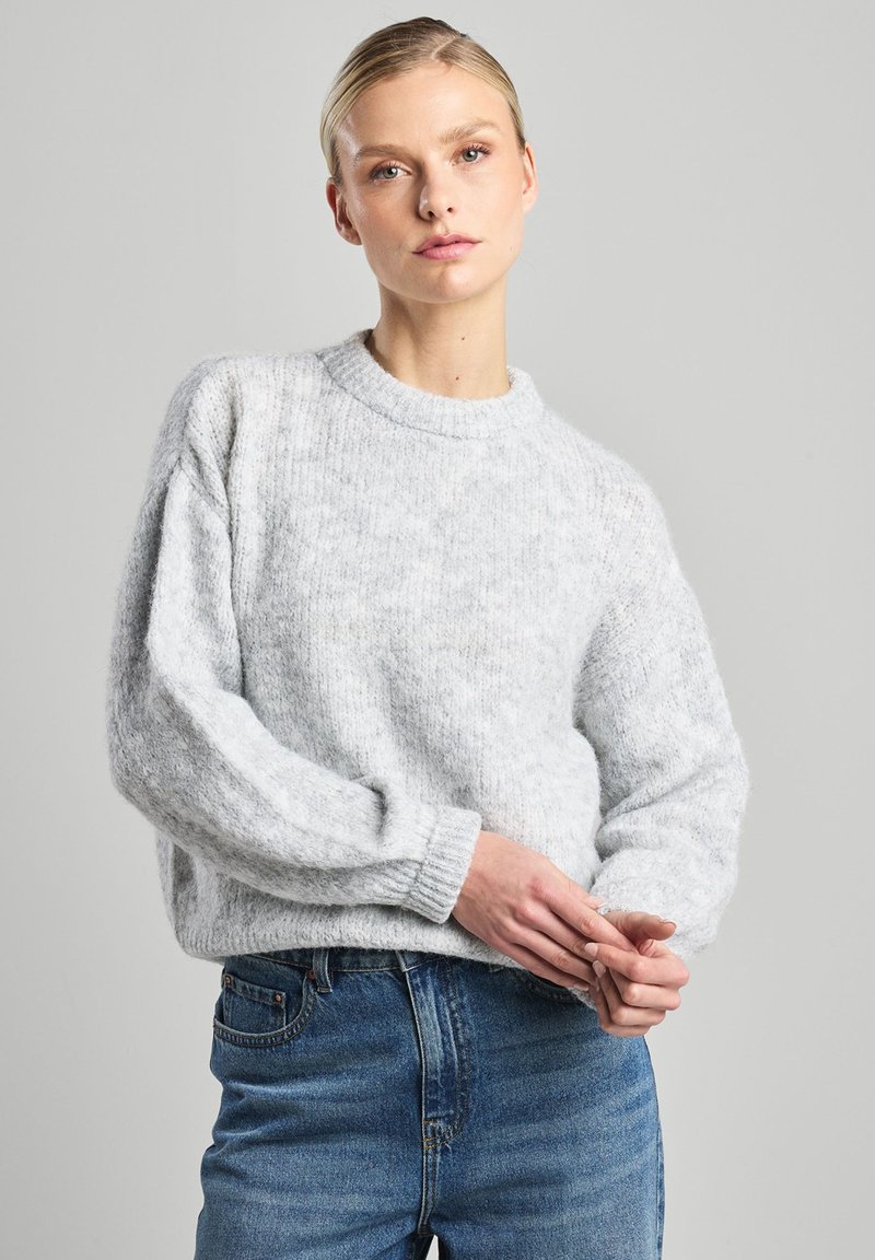 Light gray knit sweater with a round neckline and dropped shoulders. Soft texture with ribbed cuffs and hem. Paired with blue denim jeans.