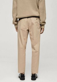 Beige op maat gemaakte broek met een rechte snit, met twee achterzakken. Draag het met een gestructureerd bruin gebreid sweater en zwarte schoenen.