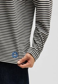 Schwarz-weiß gestreift, langärmliges Hemd mit einem blauen Logo am Saum, lockere Passform und weichem, strukturiertem Stoff.