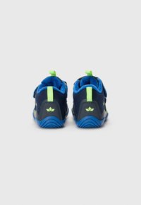 Navyblaue Schuhe mit einem flauschigen blauen Futter, grünen Akzenten und Klettverschlüssen; ausgestattet mit einer strukturierten Sohle und einer Zuglasche an der Rückseite für einfaches Anziehen.