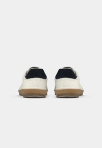 Witte leren sneakers met marineblauwe suède details en een gumzool, met een strakke uitstraling en gestikte accenten op de achterkant.