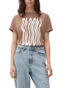 Hnědé bavlněné tričko s oversized střihem, zdobené bílým fluidním grafickým potiskem. Kombinováno se světlými modrými džínami s vysokým pasem.