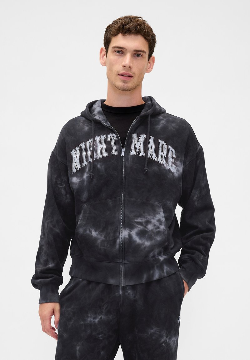 Sweatshirt com fecho de correr, padrão tie-dye preto, com a palavra "NIGHTMARE" impressa em letras brancas e em negrito. Apresenta um bolso frontal tipo pouch e capuz ajustável.