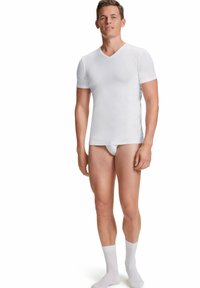 T-shirt blanc à manches courtes en V, fabriqué en tissu lisse, de coupe ajustée, porté avec des sous-vêtements blancs et des chaussettes de longueur mi-mollet.