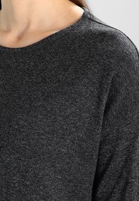 Dunkelgrauer Pullover mit rundem Halsausschnitt und langen Ärmeln, aus weichem, strukturiertem Strickstoff hergestellt. Einfaches, minimalistisches Design.