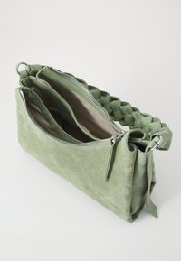 Bolsa de camurça verde com uma alça trançada, fecho de zíper prateado e compartimentos interiores. Superfícies lisas e texturizadas.