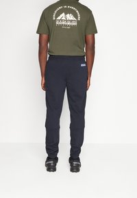 Donker marineblauwe sportbroeken met een elastische tailleband en van onderen omgeslagen pijpen, gecombineerd met een olijfgroene t-shirt met een bergafbeelding en tekst.