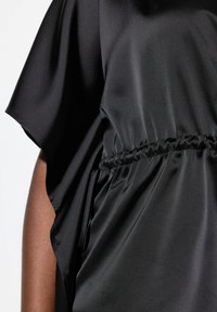 Top in satin nero con design ampio, maniche larghe e dettaglio arricciato in vita. Texture liscia con un leggero luccichio.