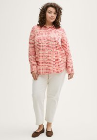 Chemise à manches longues avec un motif �à carreaux rose et rouge, associée à un pantalon blanc et des chaussures marron. Tissu doux et coupe décontractée.