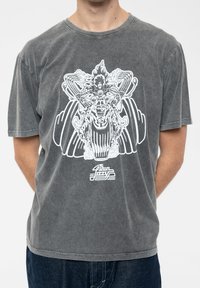 Gray cotton t-shirt with a loose fit, featuring a white graphic design of a motorcycle rider with wings and text below. Short sleeves.