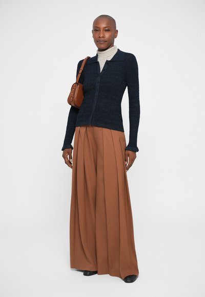 Cardigan en maille texturée marine avec des boutons, associé à un pantalon large marron. Accessoirisé avec un petit sac à épaule marron et un col roulé rayé.