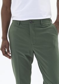 Pantalones verdes de tela suave con corte ajustado, que cuentan con un bolsillo frontal, cierre de botón y trabillas para cinturón.