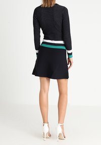 Pull en tricot noir avec des rayures horizontales blanches et vertes à l'ourlet, associé à une jupe noire évasée et des sandales à talons blanches.