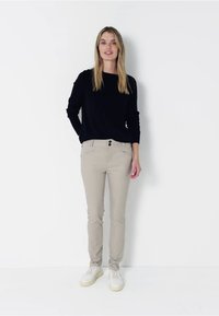 Černý dlouhý rukáv, béžové slim-fit kalhoty a bílé tenisky s žlutými akcenty; jednoduchý design s knoflíky na kalhotách.