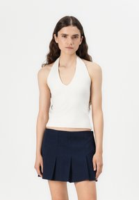 White halter top with a V-neck design, fitted style, paired with a pleated navy skirt. Smooth fabric with a simple aesthetic.