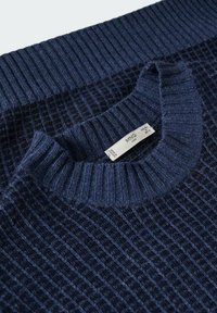 Pull bleu marine avec une texture côtelée et un col rond. Étiquette visible indiquant la taille et la marque.