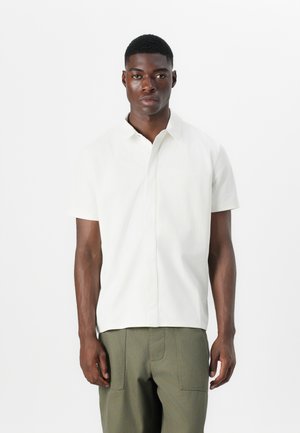 Kortærmet skjorte med knapper i off-white stof med en glat tekstur, der har en spidse krave og en afslappet pasform.