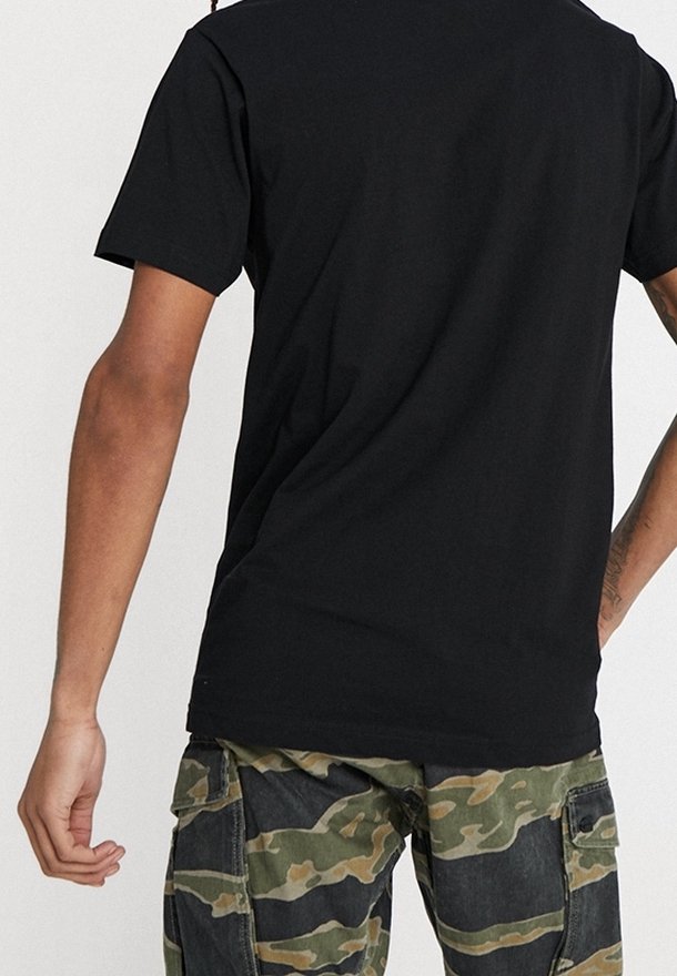 T-shirt noir à manches courtes en coton, coupe décontractée, avec un design épuré. Associé à un pantalon cargo camouflage vert avec des poches.