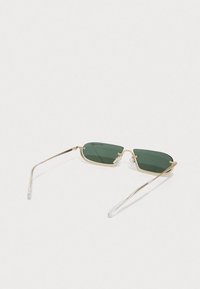 Ochelari de soare din metal cu ramă aurie, lentile verzi și capete de brațe transparente. Formă unghiulară cu un design minimalist și detalii hardware subtile.
