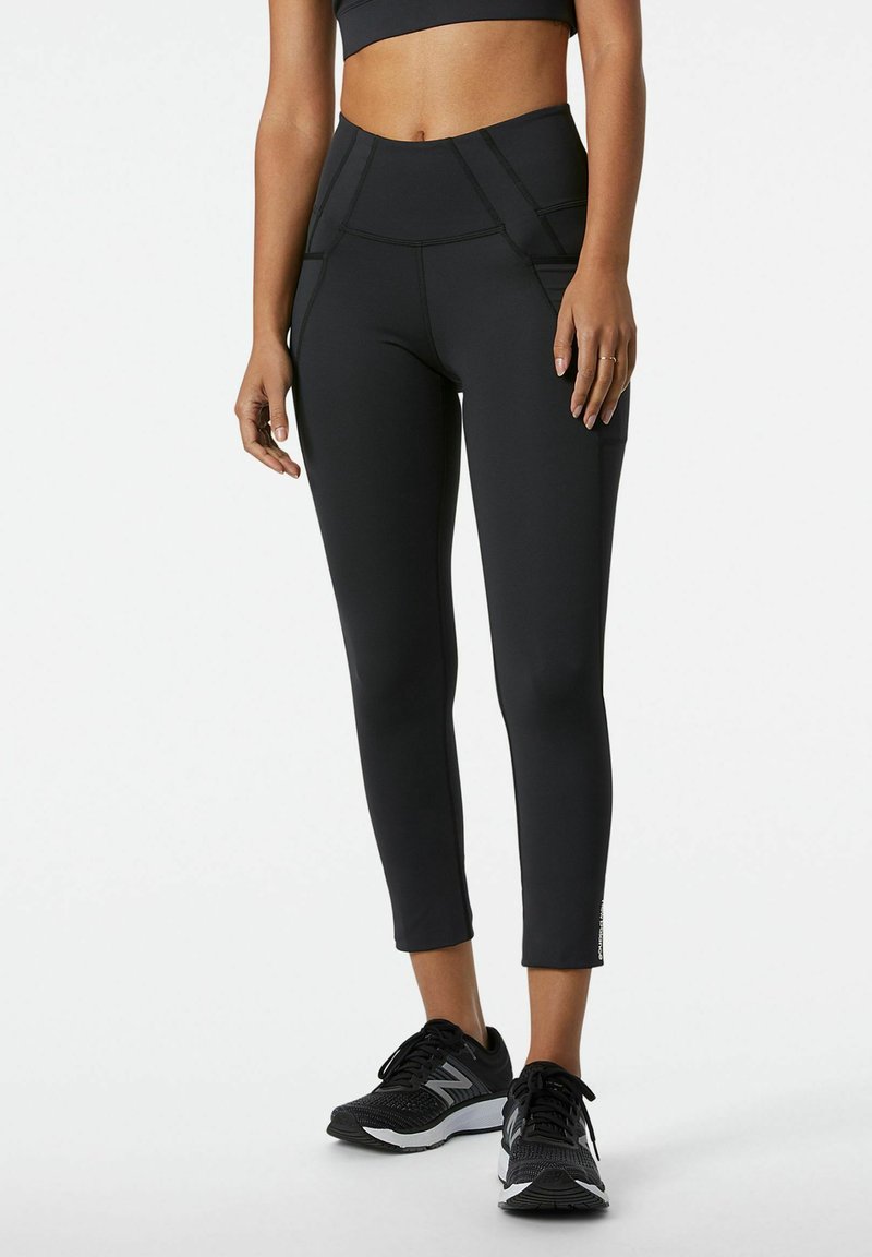 Leggings neri a vita alta realizzati in tessuto elasticizzato, caratterizzati da un design elegante, cuciture piatte e lunghezza cropped. Indossati con scarpe da ginnastica nere.