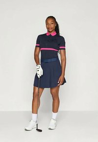 Tumes sinine golfiriietus, mis koosneb volditud seelikust ja lühikeste varrukatega polo-särgist roosade aktsentidega. Valged jalanõud ja kindad täiendavad välimust.