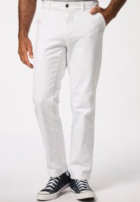 Pantaloni bianchi in cotone dal taglio slim, con passanti per cintura e chiusura con bottone anteriore. Indossati con sneakers in tela blu con dettagli bianchi.